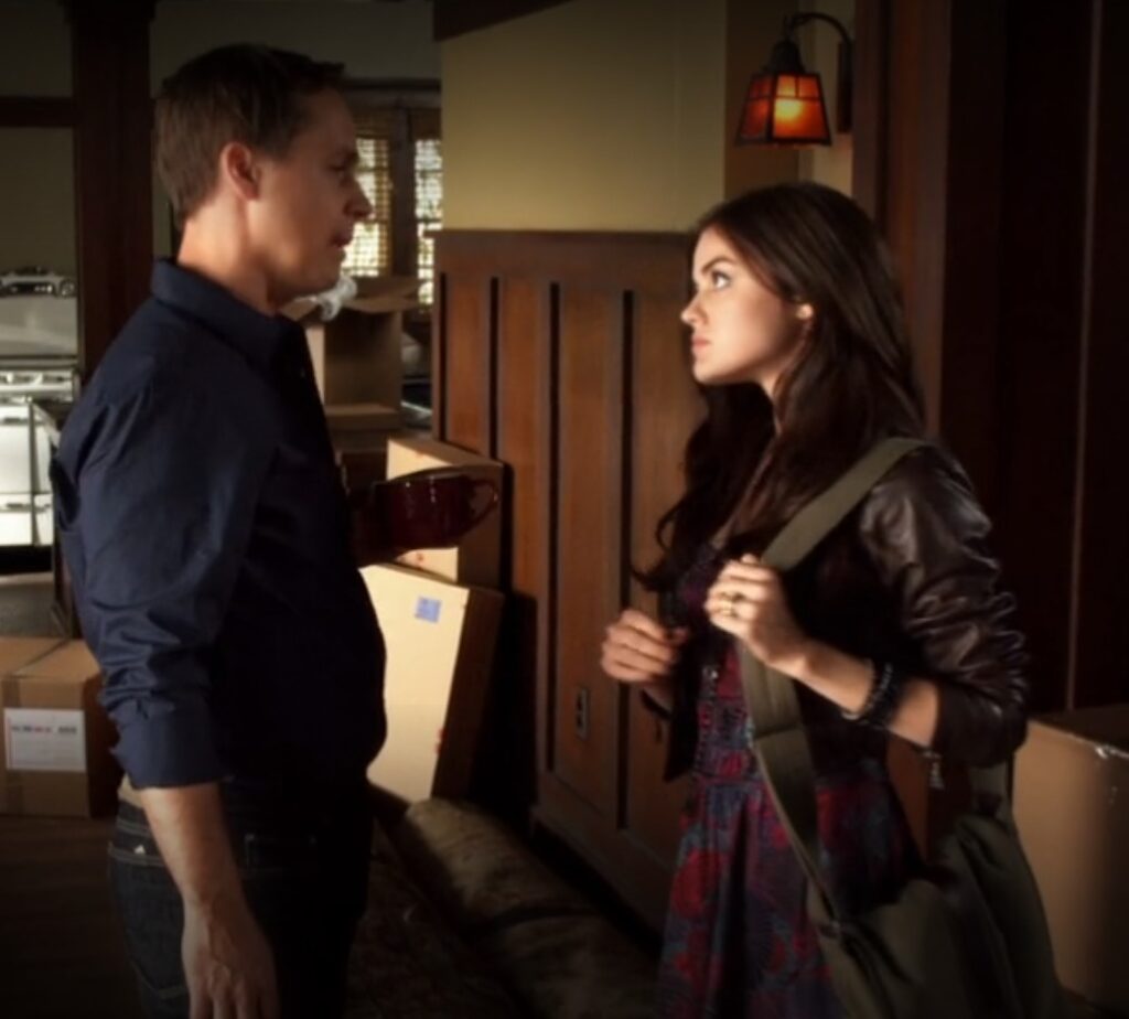 Aria and her father Byron are in the middle of a tense conversation. Aria is now wearing a black leather jacket over her dress and carrying a satchel.