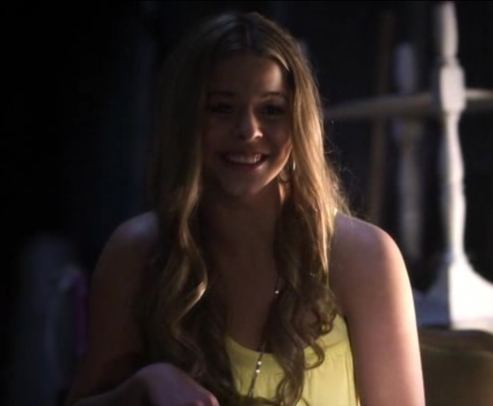 Alison sitting in a dark space and laughing while wearing a yellow top.