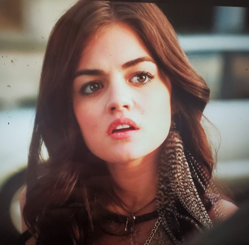 Close-up of Aria to show her single earring that has long brown and white feathers, long enough that they go past her shoulder