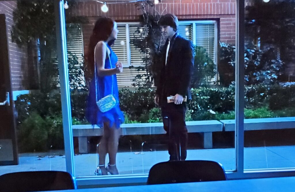 Wide shot of Emily and Toby talking outside the school, showing Emily’s cute blue dress as well as her silver purse and shoes