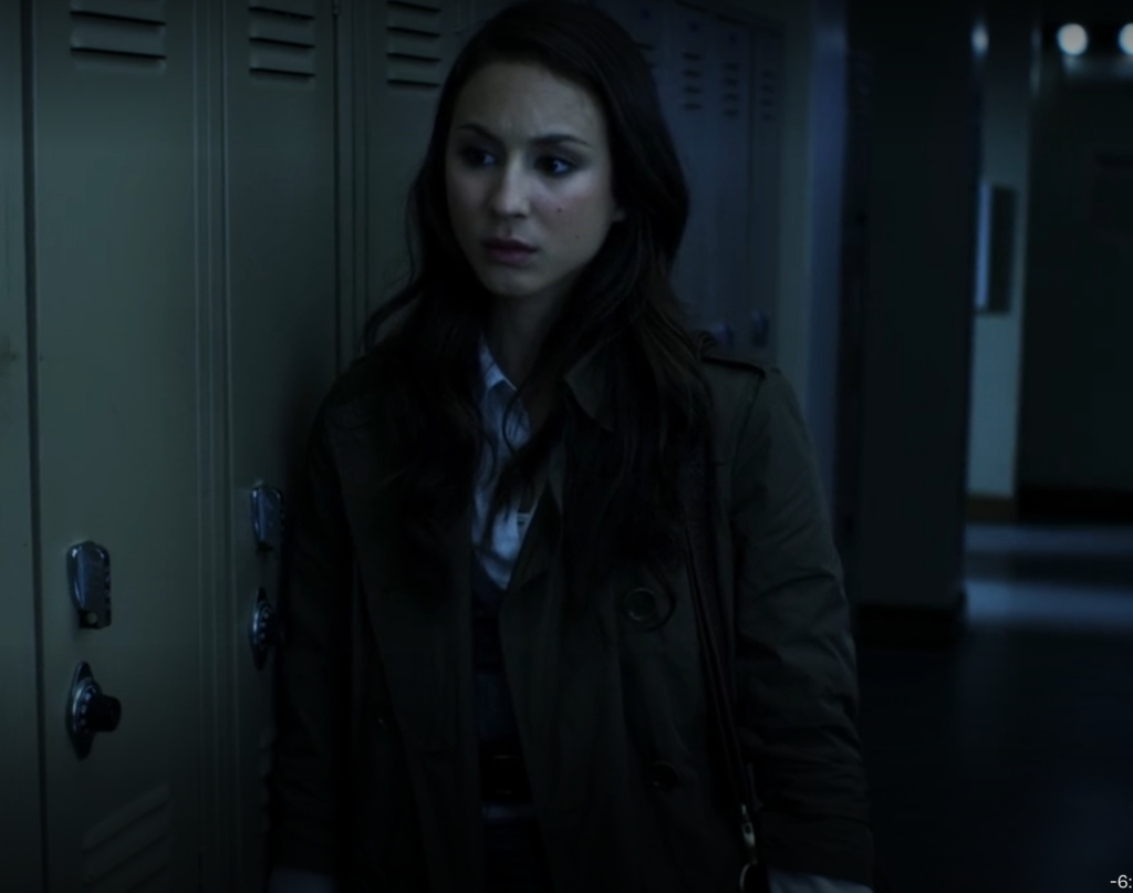 Closer shot of Spencer standing next to lockers looking concerned; the lights are out so it’s a little harder to see the outfit but we see it from the waist up.