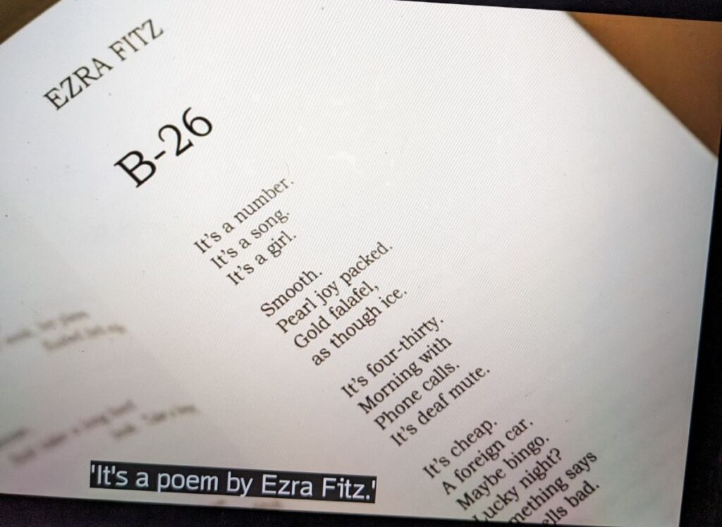Open page in a book that reads:

EZRA FITZ

B-26

It's a number.
It's a song.
It's a girl.

Smooth.
Pearl joy packed. 
Gold falafel,
as through ice.

It's four-thirty.
Morning with
Phone calls.
It's deaf-mute.

It's cheap.
A foreign car.
Maybe bingo.
Lucky night?
Something says
[words cut off] ells bad.

The subtitle over the image says, "It's a poem by Ezra Fitz."