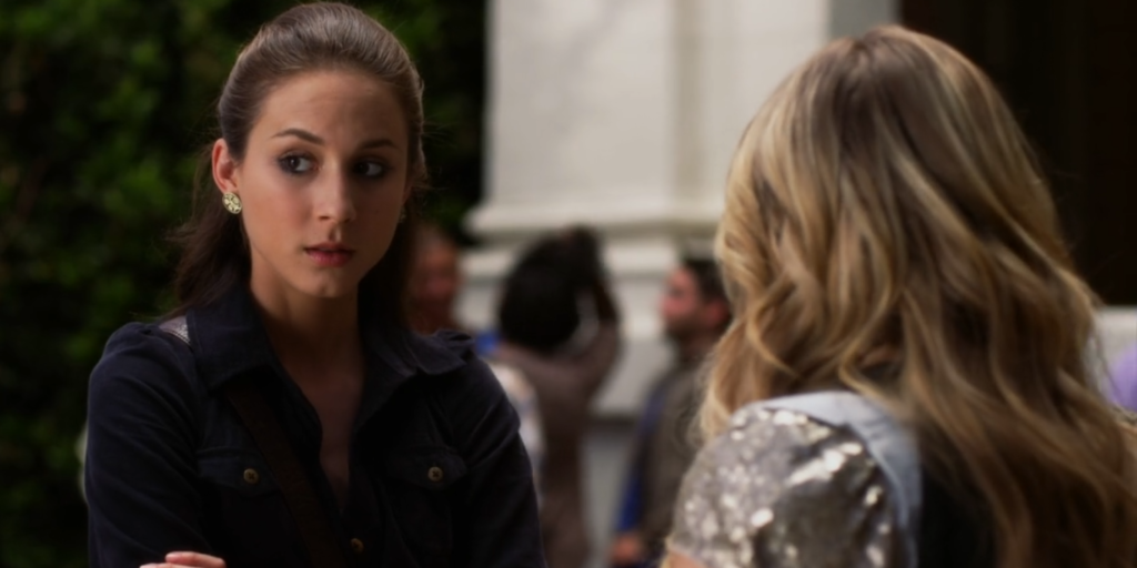 Spencer talking to Hanna (whose back is to the screen) at school. We can only see her from the chest up, and she’s wearing round earrings with her hair in a half-updo.