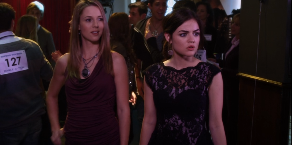 Aria and Simone at the school dance, where we can see Aria’s black lacy dress from the waist up; it has flower-like patterns and she is wearing some kind of light colored slip underneath. She is looking offscreen, the expression on her face angry, while Simone is looking at the same thing, amused.