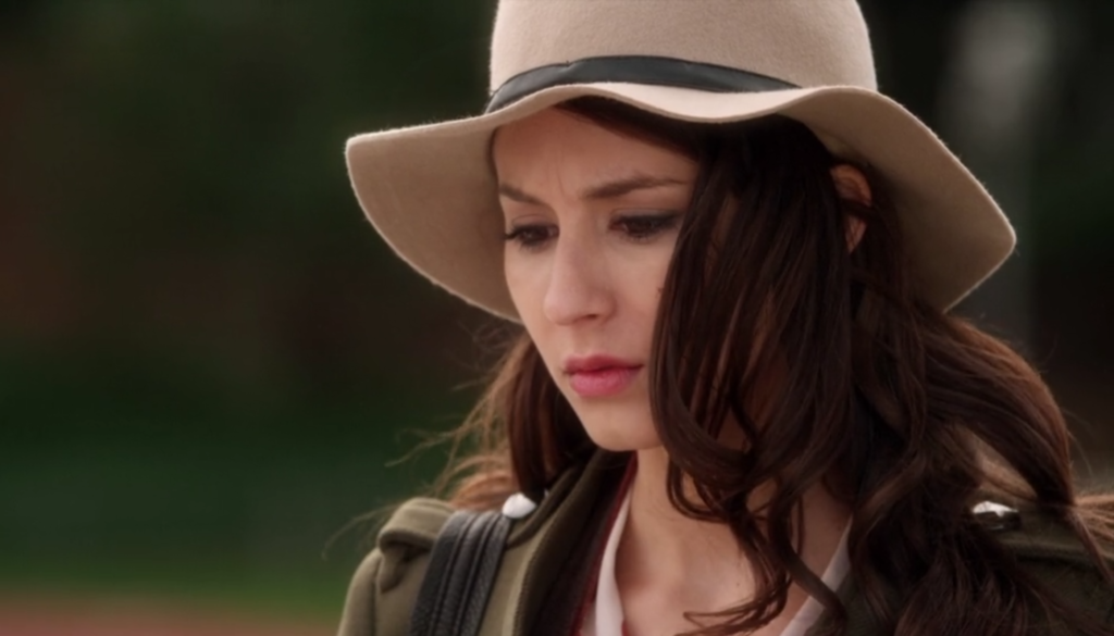 Close-up of Spencer looking down contemplatively. She’s wearing a cream colored sun hat with a black ribbon around it. Her hair is loose beneath the hat and is blowing into her face a little.