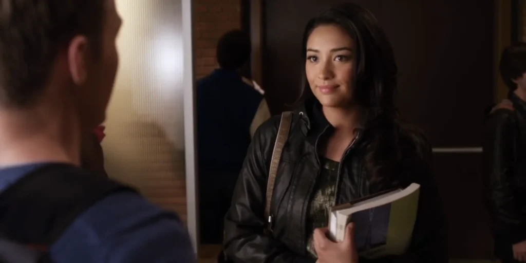 Emily is wearing a black leather jacket with a hood over a top that can barely be seen, but is also dark with some kind of shimmery silver pattern.