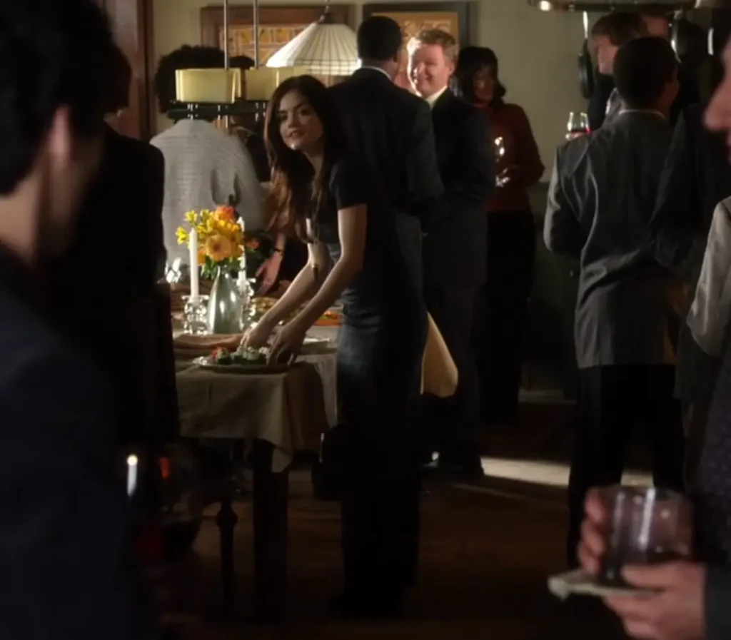 Far shot of Aria serving food during a party at her house. She is wearing a dark, short-sleeved, floor-length, form-fitting dress.