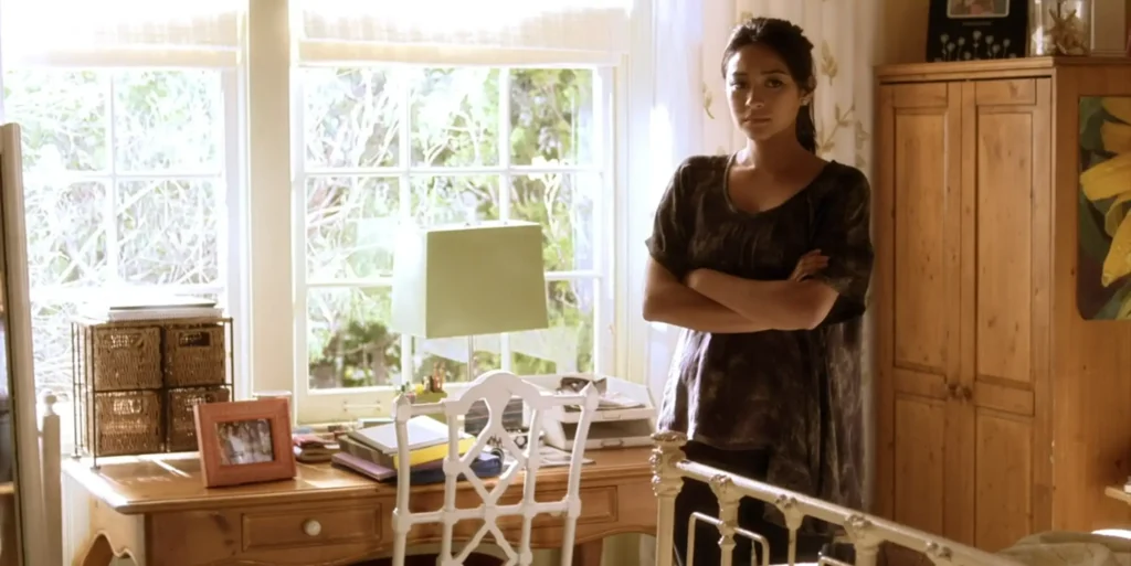 Emily is standing in her bedroom looking concerned, wearing an 2.01 Image 06oversized gray top with splotches of lighter gray. The shirt hangs low in an asymmetrical way.