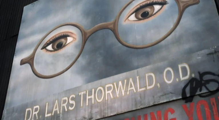 Old, worn billboard with a giant pair of disembodied eyes with glasses, reading “Dr. Lars Thorward, O.D.”