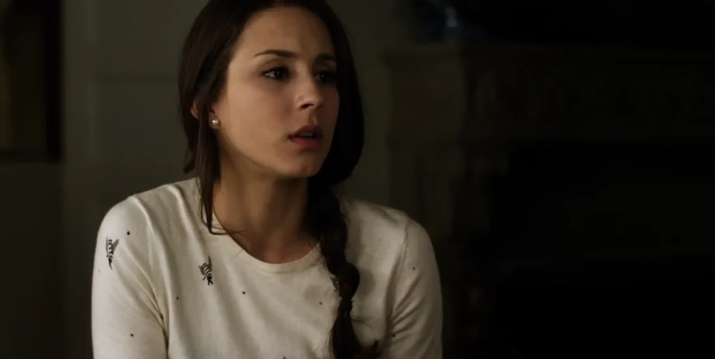 Close-up of Spencer looking concerned; she is wearing a white long-sleeved shirt that has little bees on it