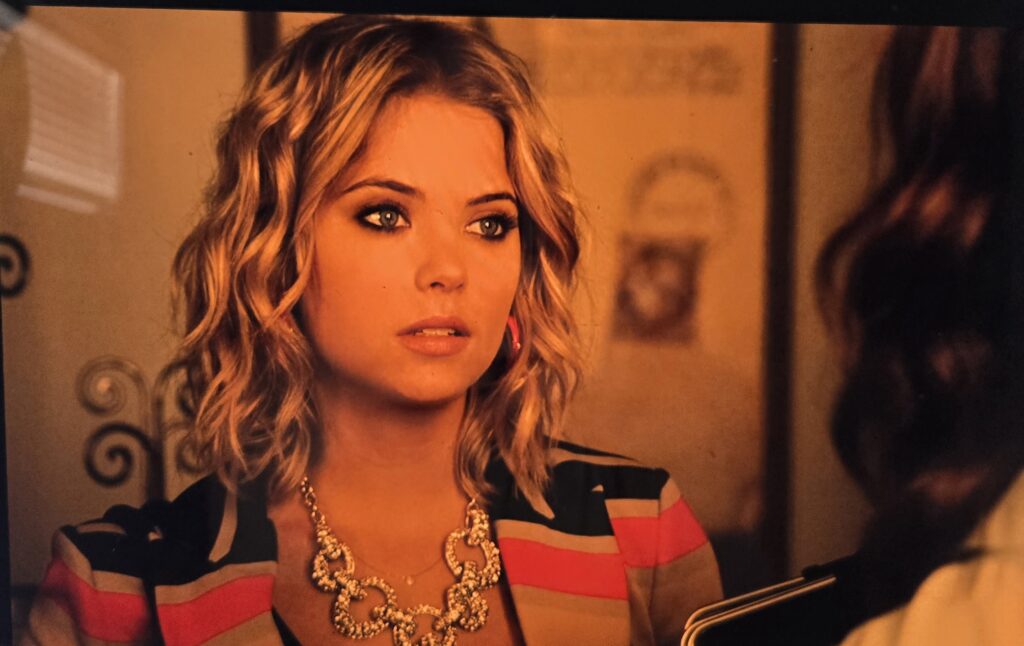 Hanna wearing a striped multi-colored blazer and a large chunky necklace with big silver glittery links