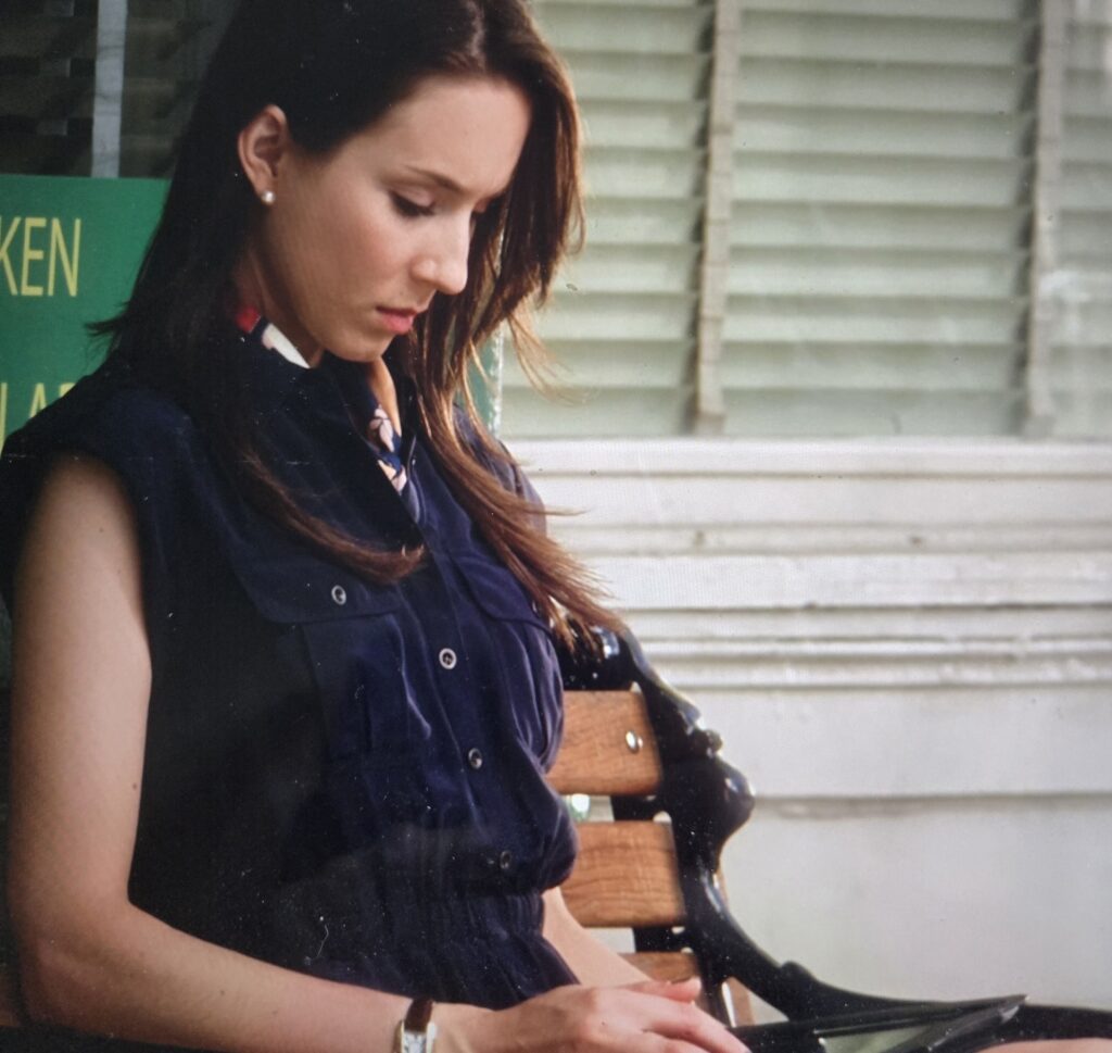 Spencer glancing down wearing a navy blue romper and a multi-colored scarf tied around her neck