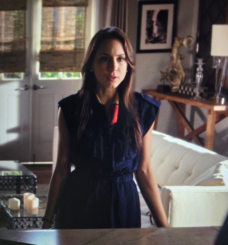 Spencer standing in her kitchen in a navy blue romper with a multi-colored scarf tied around her neck