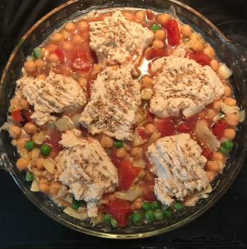 A dish with chickpeas, tomatoes, and peas topped with small unbaked gluten-free biscuits