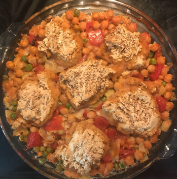 A dish with chickpeas, tomatoes, and peas topped with small baked gluten-free biscuits