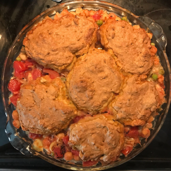 A dish with chickpeas, tomatoes, and peas topped with small baked biscuits