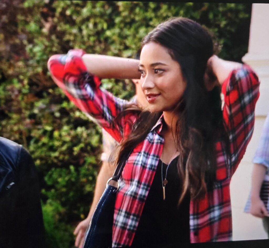 Emily looking gay in a red flannel and black tee shirt under it- she has her hands in her hair and she’s talking to Hanna after school