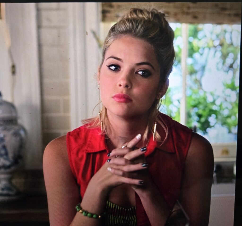 Hanna sitting down clasping her hands looking pensive. Her hair looks like almost a mullet but in a bad way.