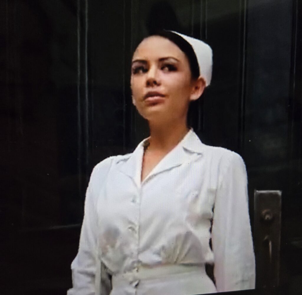Mona walking out the front door of Radley in a white nurse dress and cap