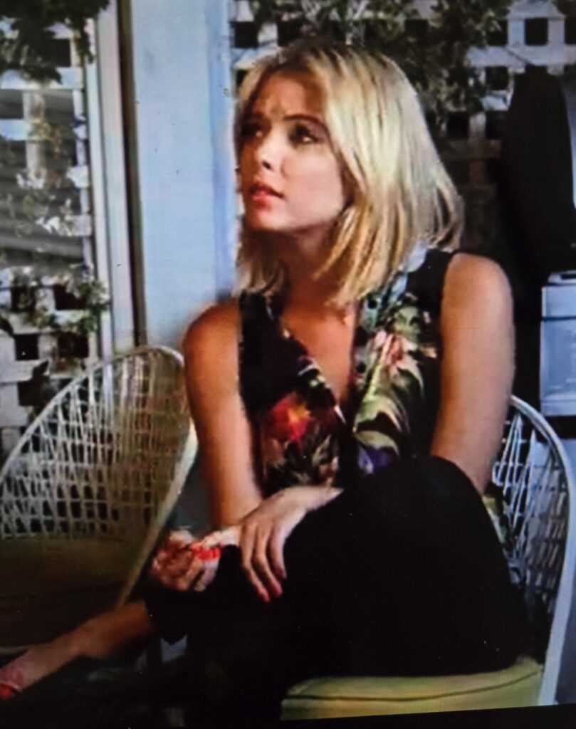 Hanna sitting down and looking concerned in black leggings and a black tank top with colorful flowers on it.