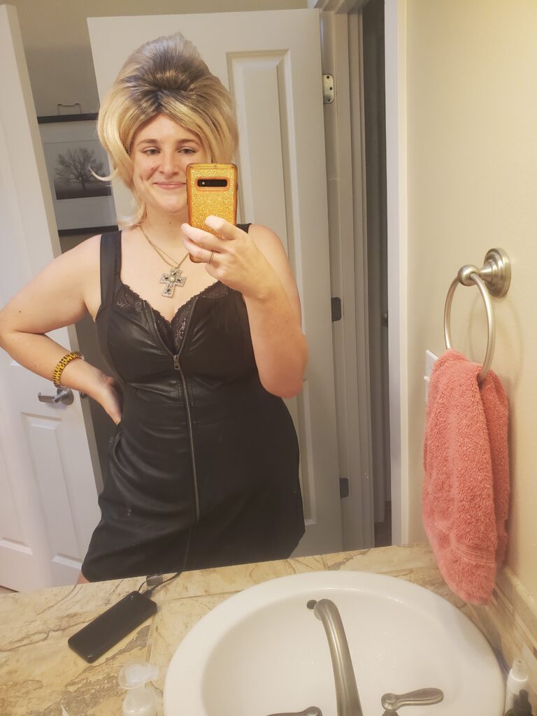 Cameron dressed up as a slutty Long Island Medium wearing a ridiculously tall wig, a leather dress, and a large cross necklace