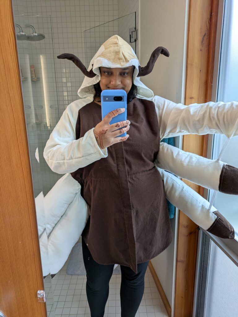 Front of Deepa's costume of Appa from Avatar: The Last Airbender, which is a modified hoodie with a brown front and white everywhere else, with horns and the beige arrow on the hood, and extra legs that are stuffed and hang off the sleeves